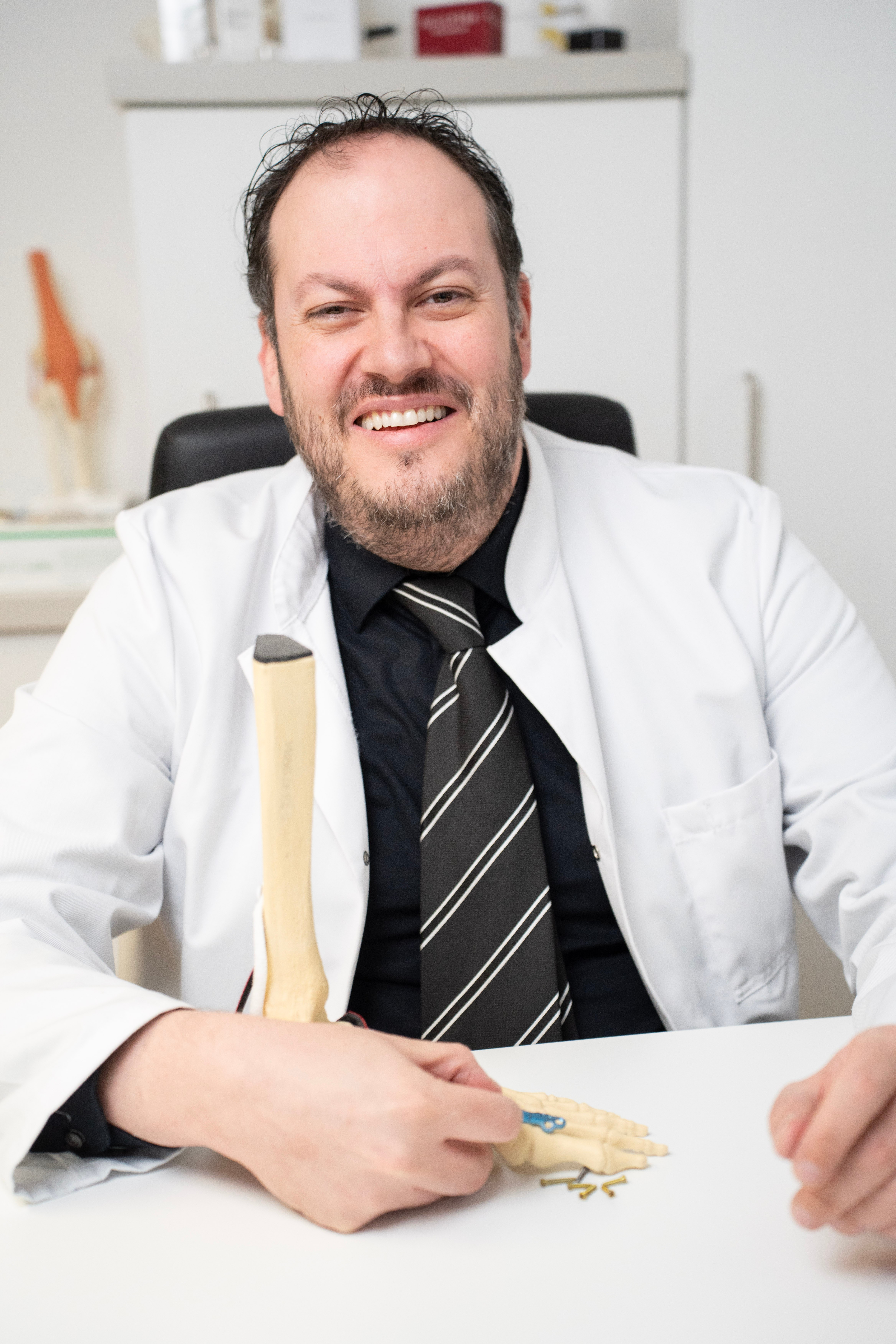 Dr. Velickovic am Schreibtisch mit Fußskelett-Modell und Implantat
