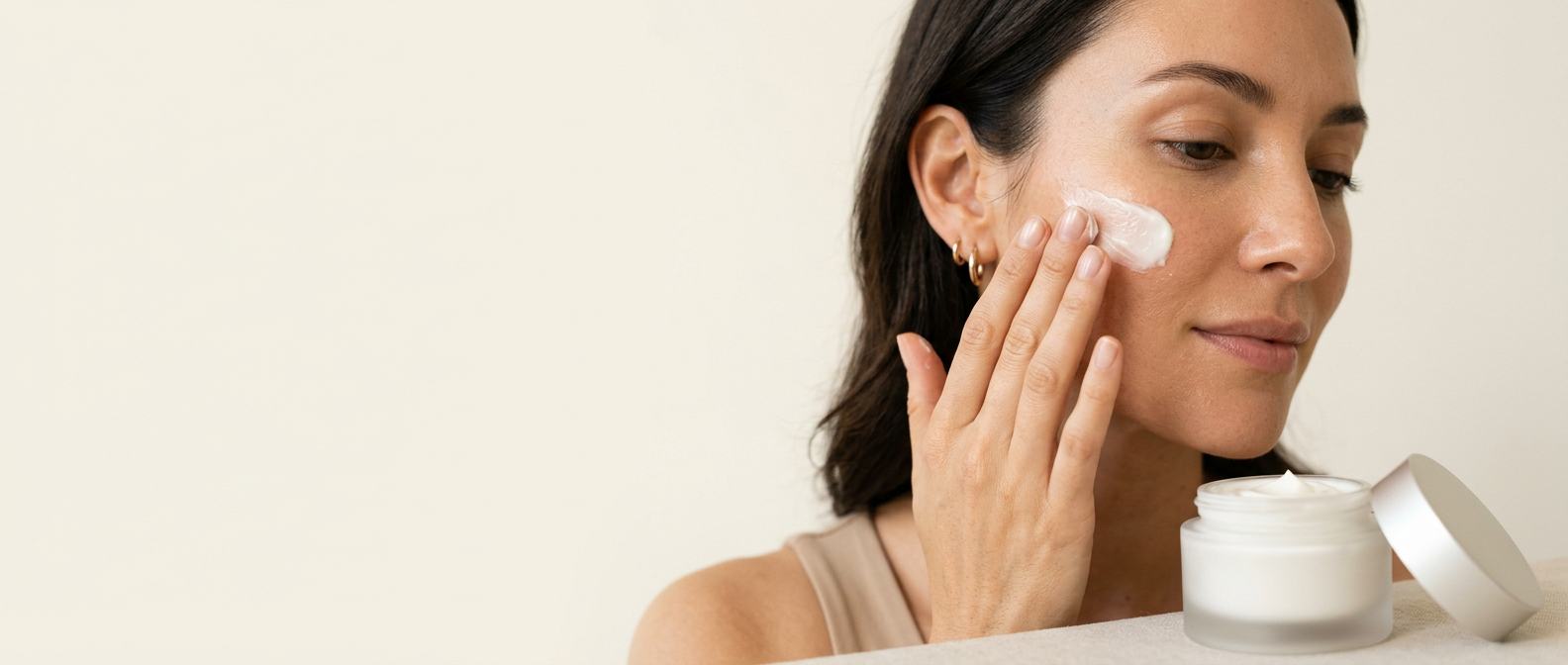 Fingerspitzen tragen eine reichhaltige Creme auf die Wange einer Frau auf